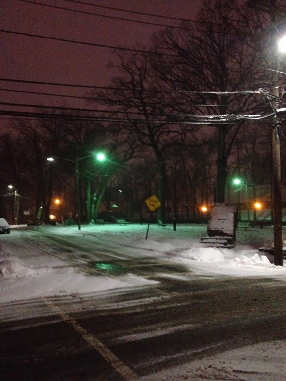 A desolate, snow-covered park with a pink sky, green streetlights, and a dead end sign.